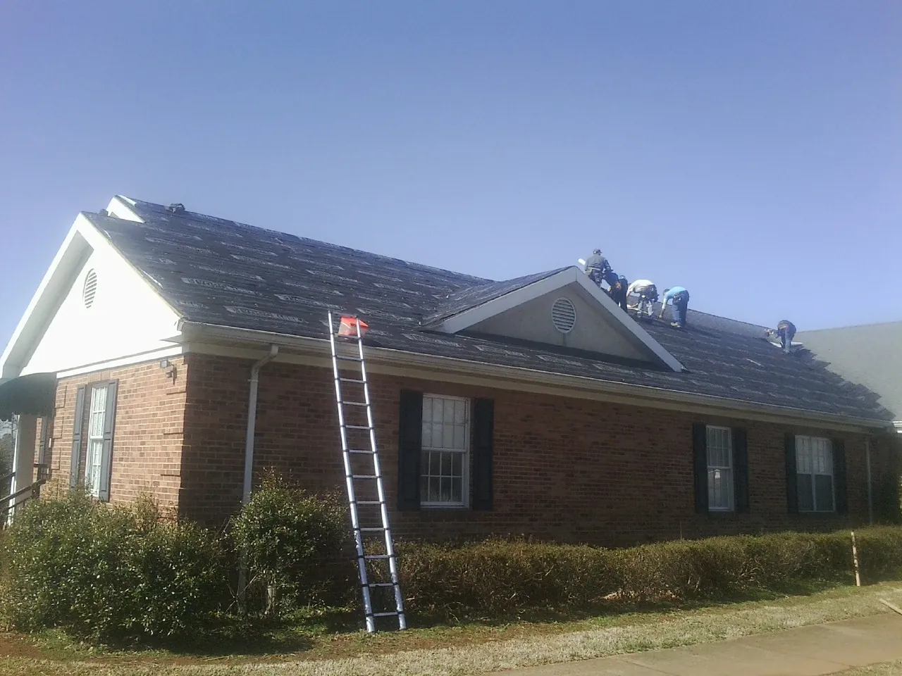 Crew tearing shingles off a brick ranch roof with a ladder set — Emergency Roof Repair work by our crew in Lake Andes