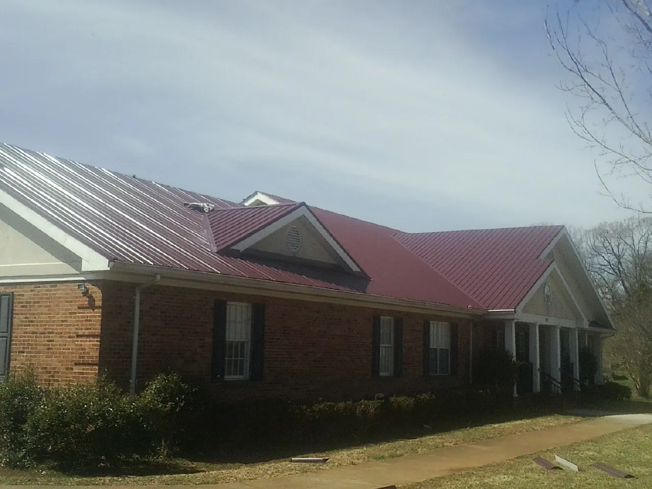 Red metal roof with gabled entries on a long brick building, from a Hail Damage Roof Repair job in Lake Andes