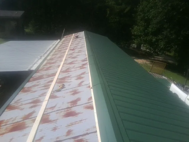 Old rusted panels beside newly installed green metal roofing — Wind Damage Roof Repair by Roofing Brothers in Lake Andes