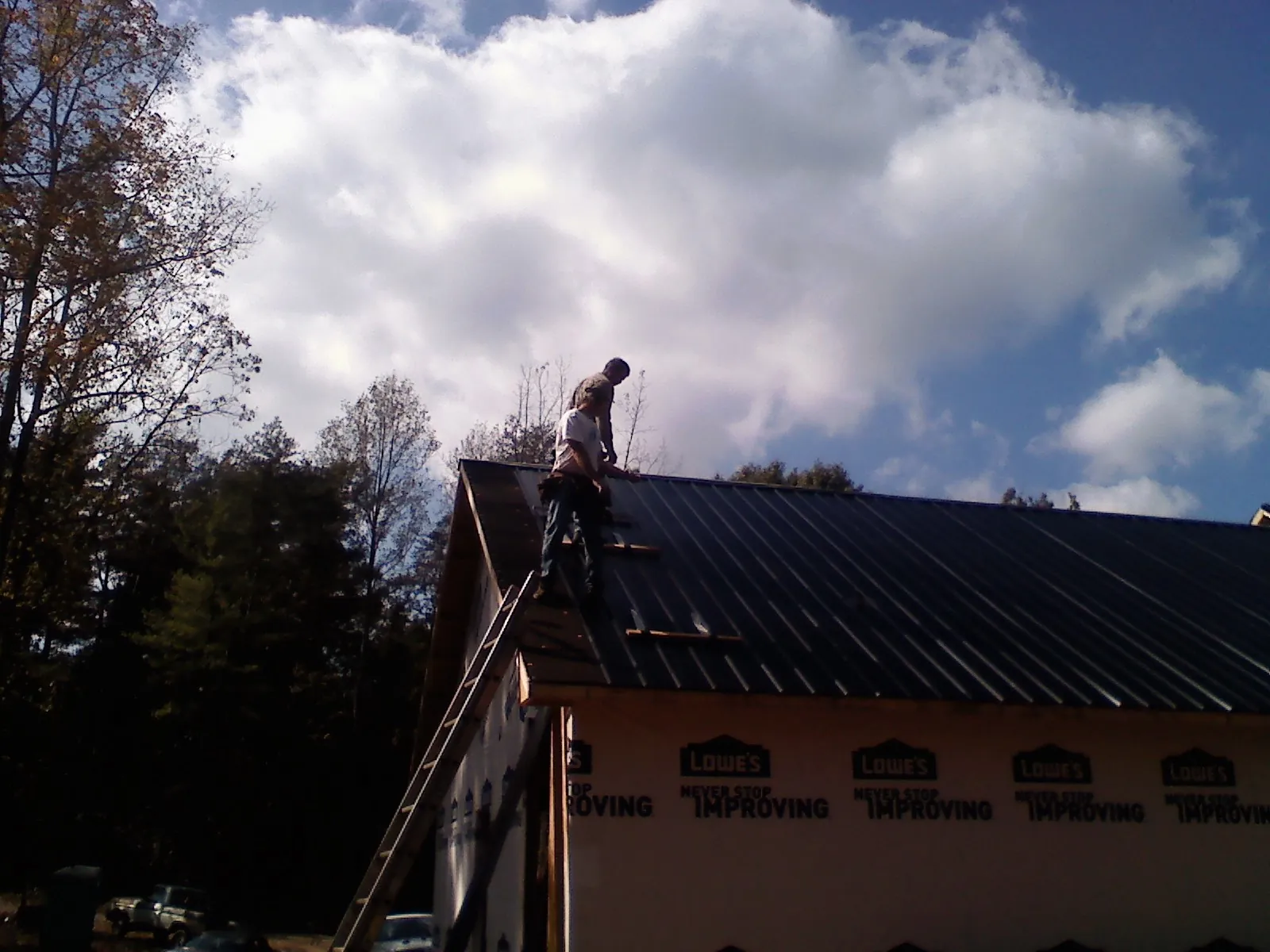Roofer fastening dark metal panels high against a cloudy sky, from a Roof Inspection job in Lake Andes