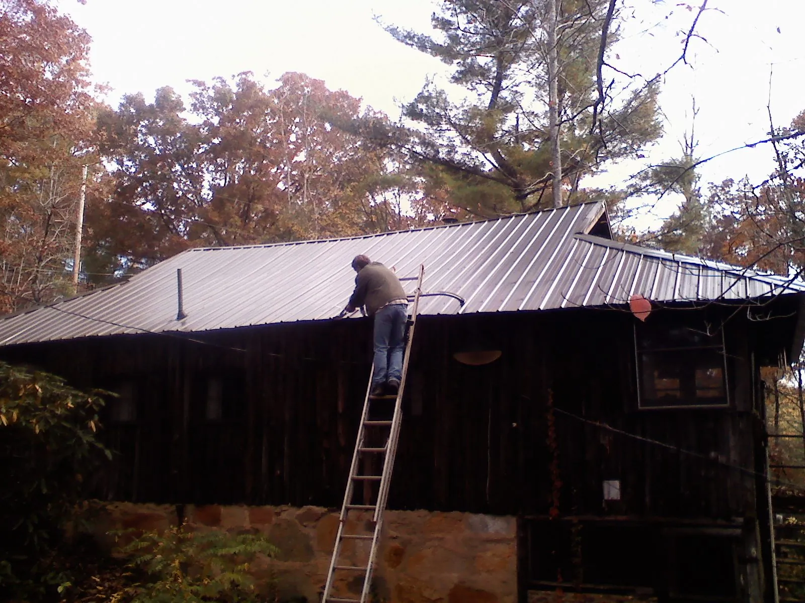 Roofer on a ladder working along the edge of a cabin metal roof in Lake Andes