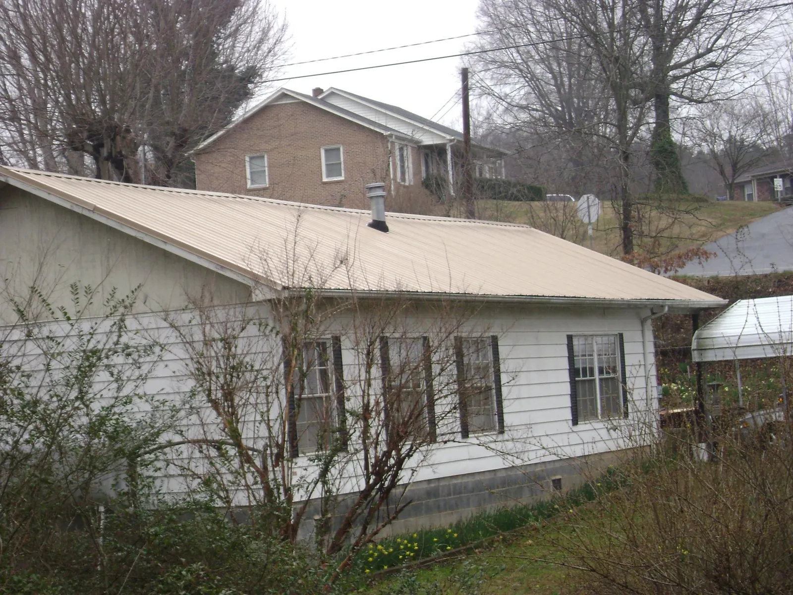 Tan metal roof on a white sided house set into a hillside — Commercial Roofing by Roofing Brothers in Lake Andes